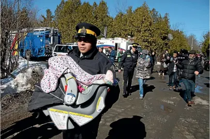  ?? PHOTO: REUTERS ?? A Royal Canadian Mounted Police officer carries a child in a car seat as the mother is escorted to a waiting vehicle after crossing the border from the United States into Hemmingfor­d, Quebec yesterday. A family of four crossed as the RCMP was...