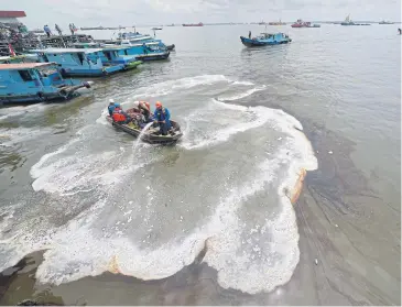  ?? AFP ?? Indonesian workers trying to clean an oil spill from the sea in Balikpapan.