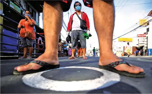  ??  ?? SOCIAL DISTANCING –Market-goers observe social distancing by following the circles painted on the street while queuing up at the Zapote Kabila Market in Bacoor, Cavite, April 17, 2020. ( Ali Vicoy)