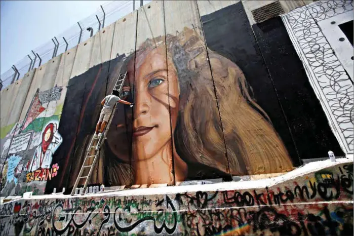  ?? FOTO: MUSSA ISSA QAWASMA / REUTERS ?? To italienske kunstnere ble kastet ut av Israel etter å ha malt dette maleriet av Ahed Tamimi på barrieren som omkranser vestbredde­n