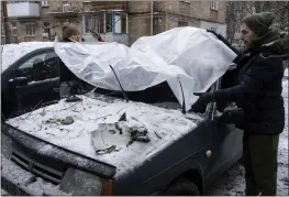  ?? EVGENIY MALOLETKA — THE ASSOCIATED PRESS ?? A couple cover their damaged car with a plastic tarp on Wednesday after a Russian attack in Kyiv, Ukraine.