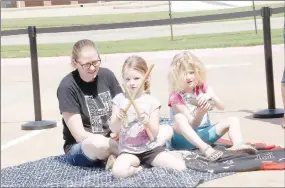  ?? ?? Allison Lane, of Farmington, watches as her children, Iris and Astraea, keep the beat with these instrument­s while listening to the percussion group, Afrique Aya, which means Africa Welcome, in front of Farmington Public Library.