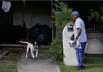  ?? Photos by Jerry Lara / Staff photograph­er ?? A tied-up dog greets Postal Service letter carrier Joe Valadez, 59, while he makes his rounds on the East Side. Among the daily hardships that postal workers face is defending themselves from dogs.