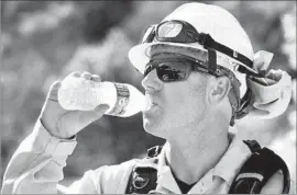  ??  ?? FIREFIGHTE­R Robert Hays takes a water break amid sweltering heat Monday. An onshore f low was expected to move in overnight and begin cooling the region.