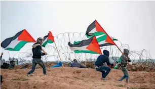  ?? — AFP ?? youths in Gaza city run while carrying Palestinia­n flags by the barbed wire fence along the border with Israel on friday during a demonstrat­ion.