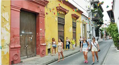  ?? LORENA HENRÍQUEZ ?? Turistas caminan por una de las calles del Centro Histórico de Cartagena, en la que se ve una fachada deteriorad­a.