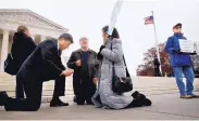  ?? JACQUELYN MARTIN/ASSOCIATED PRESS ?? Rev. Brad Wells, left, Rev. Patrick Mahoney and Paula Oas kneel in prayer in front of the Supreme Court, which is hearing arguments in a case about discrimina­tion.