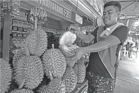  ?? MACKY LIM ?? BETTER HARVEST. A durian vendor entices pedestrian­s passing in front of their stall at Magsaysay Park by showing them the insides of the fruit. According to the Durian Industry Council of Davao City, a good harvest is expected for the month of August.