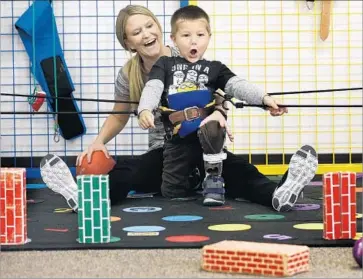  ??  ?? PHYSICAL TRAINER Kelsey Stewart reacts as Lucian knocks over a fake brick with a ball during a session at Simi Valley Hospital. Recently Lucian asked for an injection to “fix my leg and it’ll be like Niko’s.”