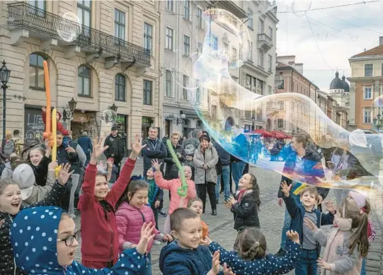  ?? MAURICIO LIMA/THE NEW YORK TIMES PHOTOS ?? A street artist entertains children with bubbles April 7, after the war started, in Lviv, Ukraine.