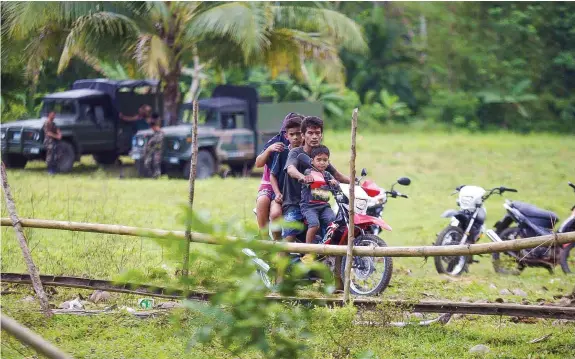  ?? JAY ROMMEL LABRA ?? A family rides on a motorcycle past military trucks in Barangay Napo, Inabanga town in Bohol where government troops clashed with members of the Abu Sayyaf last week. Authoritie­s have heightened security in the island with the ongoing ministers meeting of the Associatio­n of Southeast Asian Nations (ASEAN) in Panglao Island.