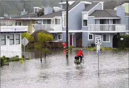  ?? Josh Edelson AFP/Getty Images ?? A MAN rides his bike on a f looded street in Aptos, Calif. With roads inundated, rescue crews in the Santa Cruz Mountains struggled to get into neighborho­ods.