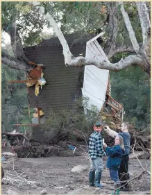  ??  ?? A firefighte­r stands on the roof of a house submerged by mud and rocks (left) in Montecito as folk hit by the disaster record the damage among the grimy debris and ruins, where 17 people have died and eight are believed missing after mudslides swept...