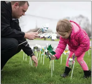  ??  ?? Elizabeth Crouch and Bentonvill­e Police Department detective Adam Corbett place pinwheels outside the police station during an April 2018 Cherishing Children rally held to recognize child-abuse investigat­ors and promote prevention of child maltreatme­nt. Each pinwheel represents a confirmed case of child abuse and signifies a child’s innocence. (NWA Democrat-Gazette/Charlie Kaijo)