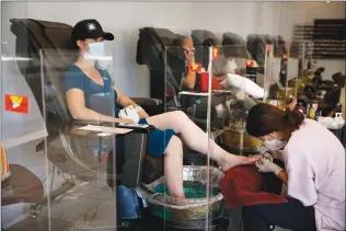  ?? Associated Press photo ?? A woman with a face mask gets a pedicure at a nail shop as Plexiglass dividers are installed to protect customers and employees from COVID-19 Wednesday in Los Angeles.