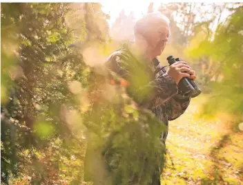  ?? FOTO: JANA BAUCH ?? Johann Liebel steht hinter einem Baum und beobachtet durch sein Fernglas. Um nicht aufzufalle­n, bleibt er versteckt und hat sich extra eine Tarnjacke übergezoge­n.