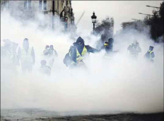 ?? Kamil Zihnioglu The Associated Press ?? Masked demonstrat­ors wearing yellow jackets appear through tear gas Saturday near the Champs-Elysees during a demonstrat­ion in Paris. Protesters have said they are angry about the country’s high cost of living.