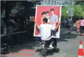  ?? ZHANG JUSHENG / FOR CHINA DAILY ?? A man carries a photo of a happy family on the back of an electric bicycle in Neiwubu Street, Dongcheng district, Beijing, on June 8, 2012.