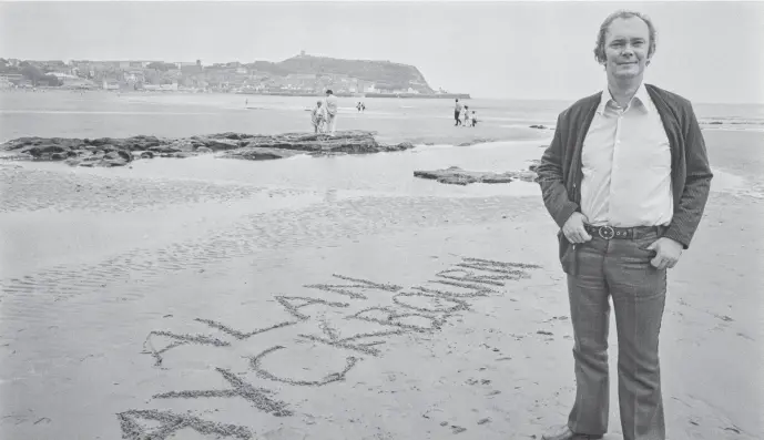  ?? ?? Go with the grains: Alan Ayckbourn on the beach at Scarboroug­h with his name written in the sand.
Picture: Evening Standard/Hulton Archive/Getty Images