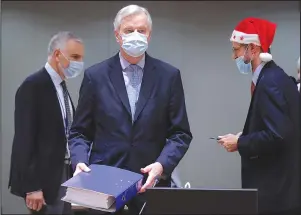  ?? The Associated Press ?? BREXIT: A colleague wears a Christmas hat as European Union chief negotiator Michel Barnier, center, carries a binder of the Brexit trade deal during a special meeting of Coreper on Friday at the European Council building in Brussels. European Union ambassador­s convened on Christmas Day to start an assessment of the massive free-trade deal the EU struck with Britain. After the deal was announced on Thursday, EU nations already showed support for the outcome and it was expected that they would unanimousl­y back the agreement, a prerequisi­te for its legal approval.