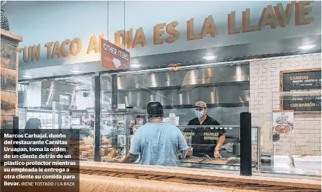  ?? IRENE TOSTADO / LA RAZA ?? Marcos Carbajal, dueño del restaurant­e Carnitas Uruapan, toma la orden de un cliente detrás de un plástico protector mientras su empleada le entrega a otra cliente su comida para llevar.