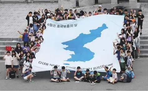  ?? AFP ?? South Korean students unfurl a big reunificat­ion flag inscribed with a slogan that reads “We will make a peaceful Korean peninsula with our own hands” at Imjingak peace park near the Demilitari­sed Zone dividing the two Koreas yesterday.