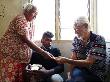  ??  ?? Generous heart: Kamala (left) handing Yap a biscuit in the rented home they share, while her grandson Thinagaran looks on.