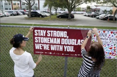  ?? SUSAN STOCKER — SOUTH FLORIDA SUN-SENTINEL VIA AP ?? Volunteers hang banners around the perimeter of Marjory Stoneman High School in Parkland, Fla., to welcome back students who will be returning to school Wednesday two weeks after the mass shooting that killed 17 students and staff.