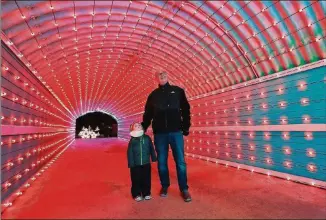  ?? CURTIS COMPTON/CCOMPTON@AJC.COM ?? Ralph Thomas and his 4-year-old grandson Logan Thomas make their way through a new tunnel of lights in Margaritav­ille at Lanier Islands in Buford.