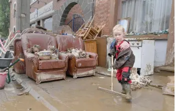  ?? — AFP photo ?? A young resident helps clean-up outside his home following heavy rains and floods in the town of Rochefort. The death toll from flooding in eastern Belgium hit 27 on July 17 as police went door-to-door seeking news of at risk residents and the prime minister toured devastated towns.