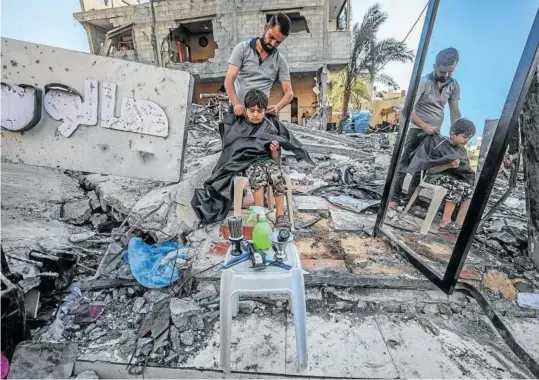  ?? Foto: Efe ?? Un barbero corta el pelo a un niño en Gaza, rodeado de escombros de lo que fue su establecim­iento antes de los bombardeos de Israel.
