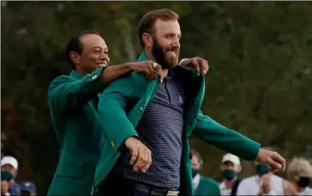  ?? AP Photo/Charlie Riedel ?? Tiger Woods helps Masters’ champion Dustin Johnson with his green jacket after his victory at the Masters golf tournament on Nov. 15 in Augusta, Ga.