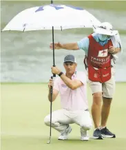  ?? Maddie Meyer / Getty Images ?? Brendon Todd balances his umbrella and his putter as he lines up a shot in the rain on his way to a 61.