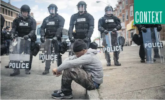  ?? ANDREW BURTON/GETTY IMAGES ?? Daquan Green, 17, sits on a curb in Baltimore on Tuesday as police stand guard after rioting that followed Monday’s funeral of Freddie Gray.