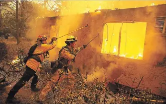  ?? JUSTIN SULLIVAN GETTY IMAGES ?? Firefighte­rs try to prevent flames from a burning home from spreading to a neighbouri­ng apartment complex Friday as they battle the Camp Fire in Paradise, Calif.