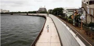  ??  ?? A man jogs on a bank along the Nakagawa River in Tokyo. — Reuters photos