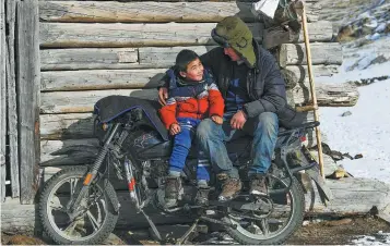  ??  ?? A boy and his father enjoy the sunshine outside the family’s log cabin.