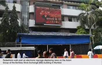  ?? Pedestrian­s walk past an electronic signage displaying news on the Adani Group at the Bombay Stock Exchange (BSE) building in Mumbai ??