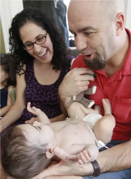  ?? PAUL CONNORS PHOTOS / BOSTON HERALD ?? OVERCOMING ADVERSITY: Lucas Pacheco smiles at his mother Alexia Orphanides and father Brett Pacheco, above, after receiving a heart transplant, far right. At right, Brett sets up Lucas’ feeding pump at their New Bedford home on Saturday.