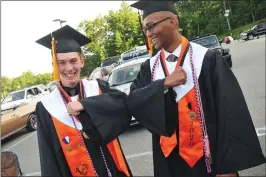  ??  ?? Above: Kevin Siefken, left, and his best friend, Nathaniel Holden, greet each other with an elbow-bump as the two arrive for graduation ceremony. Left: Katelyn Jones, left, and Maddie Ouellette help fellow graduate Max Ferrage get his cap on.