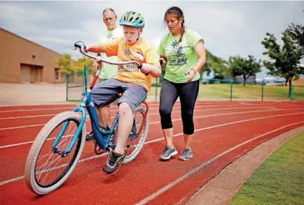  ?? [PHOTOS BY SARAH PHIPPS, THE OKLAHOMAN] ?? Bob Rook and Brianne Henichs help Reid Martin, 10, learn how to ride a bike during the iCan Bike Camp at Heritage Hall. The camp teaches people with disabiliti­es to ride a convention­al two-wheeled bicycle.