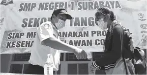  ?? FRIZAL/JAWA POS ?? PATUHI PROTOKOL: Petugas keamanan sedang memeriksa suhu tubuh siswa yang hendak masuk ke SMPN 1 Surabaya. Pemkot akan mengevalua­si simulasi sekolah tatap muka SMP.