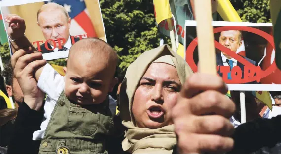  ?? AP ?? A Kurdish woman living in Cyprus holds up a baby as she shouts slogans in front of the US Embassy to protest Turkey’s offensive into Syria, in Nicosia, Cyprus, on Thursday.