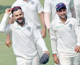  ??  ?? Indian captain Virat Kohli (L) along with teammate Kuldeep Yadav laugh as they walk back after winning the first Test cricket match against West Indies at Rajkot - AFP