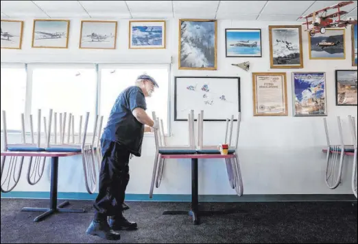  ?? Elizabeth Page Brumley Las Vegas Review-Journal @Elipagepho­to ?? Co-owner Stephen Maynard puts a sanitized chair on a table at Sunshine & Tailwinds Cafe in the North Las Vegas Airport on April 3. “We’ve had to just close up and ride this out,” Maynard said of the COVID-19 outbreak. “It’s a hard hit.”