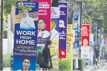  ?? ?? MASS APPEAL: A woman stands on a footpath next to the campaign posters of various parties along Phahon Yothin Road yesterday. Parties are trying to woo voters with their populist policies.