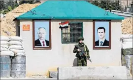  ?? Louai Beshara AFP/Getty Images ?? A MEMBER of the Russian military police is f lanked by portraits of Vladimir Putin and Syrian leader Bashar Assad on the outskirts of Damascus last month.