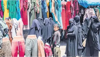  ?? ?? Women walk past a garment shop at the al-Hol camp.