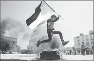  ??  ?? A Palestinia­n boy jumps with a Palestinia­n flag over a tyre burning during a reconstitu­tion performanc­e at a building which used to be an Israeli prison to hold Palestinia­ns during Israel’s occupation of Gaza, as part of a tour organized by Hamas on...