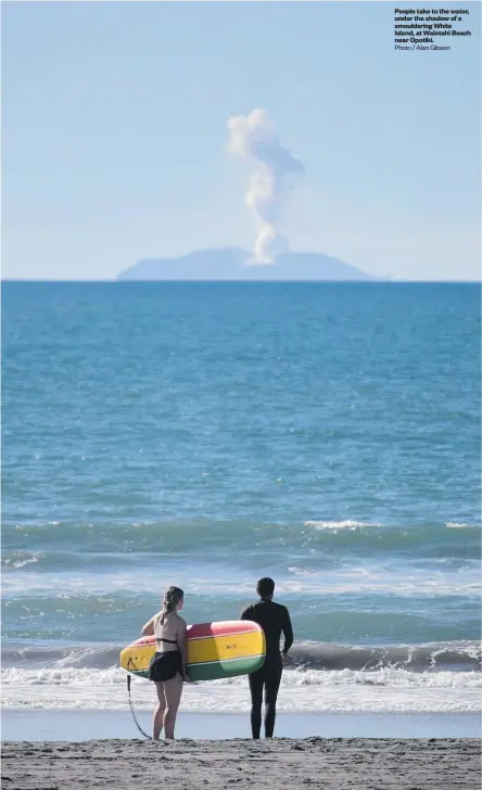  ?? Photo / Alan Gibson ?? People take to the water, under the shadow of a smoulderin­g White Island, at Waiotahi Beach near Opotiki.